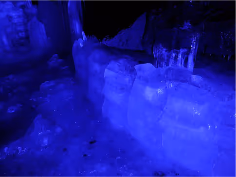Blue-lit interior of an ice cave showing thick ice formations on the ground and walls.