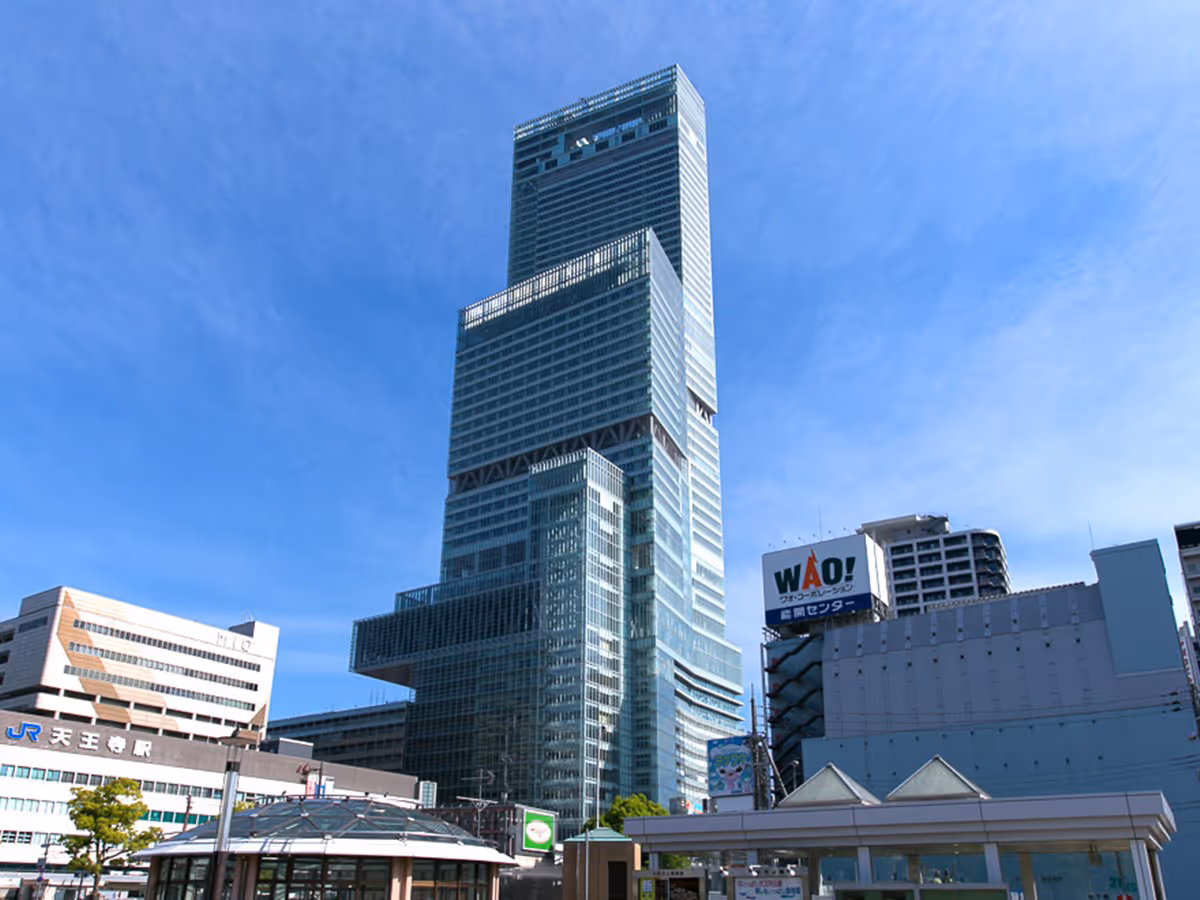Abeno Harukas skyscraper towering against a clear blue sky with surrounding buildings and signage.