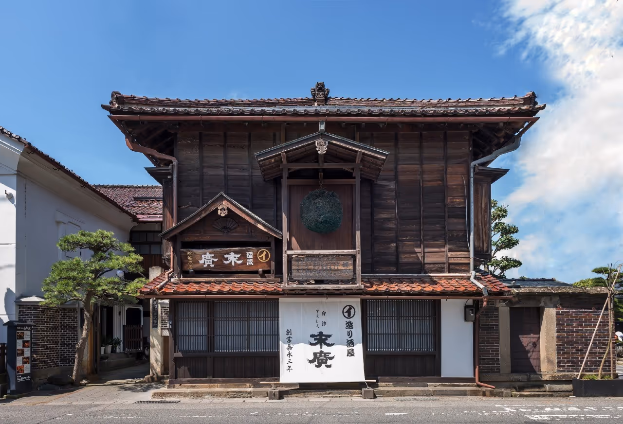 Traditional two-story Japanese wooden building with a hanging green foliage ball and white banner with black Japanese characters.