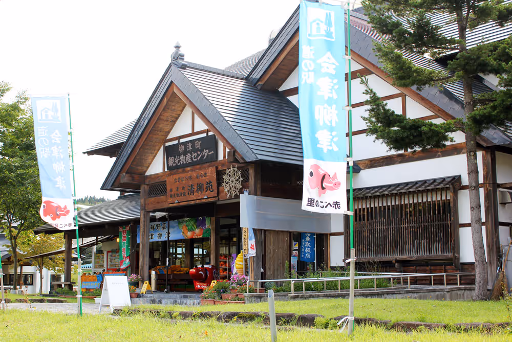 Traditional Japanese building housing a local produce center with blue banners and green grass in front.