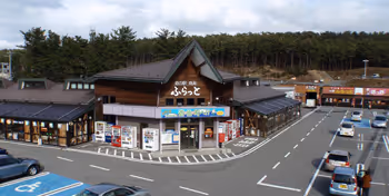 Parking lot with several cars surrounding a Japanese-style building with a steep, dark roof and wooden exterior.