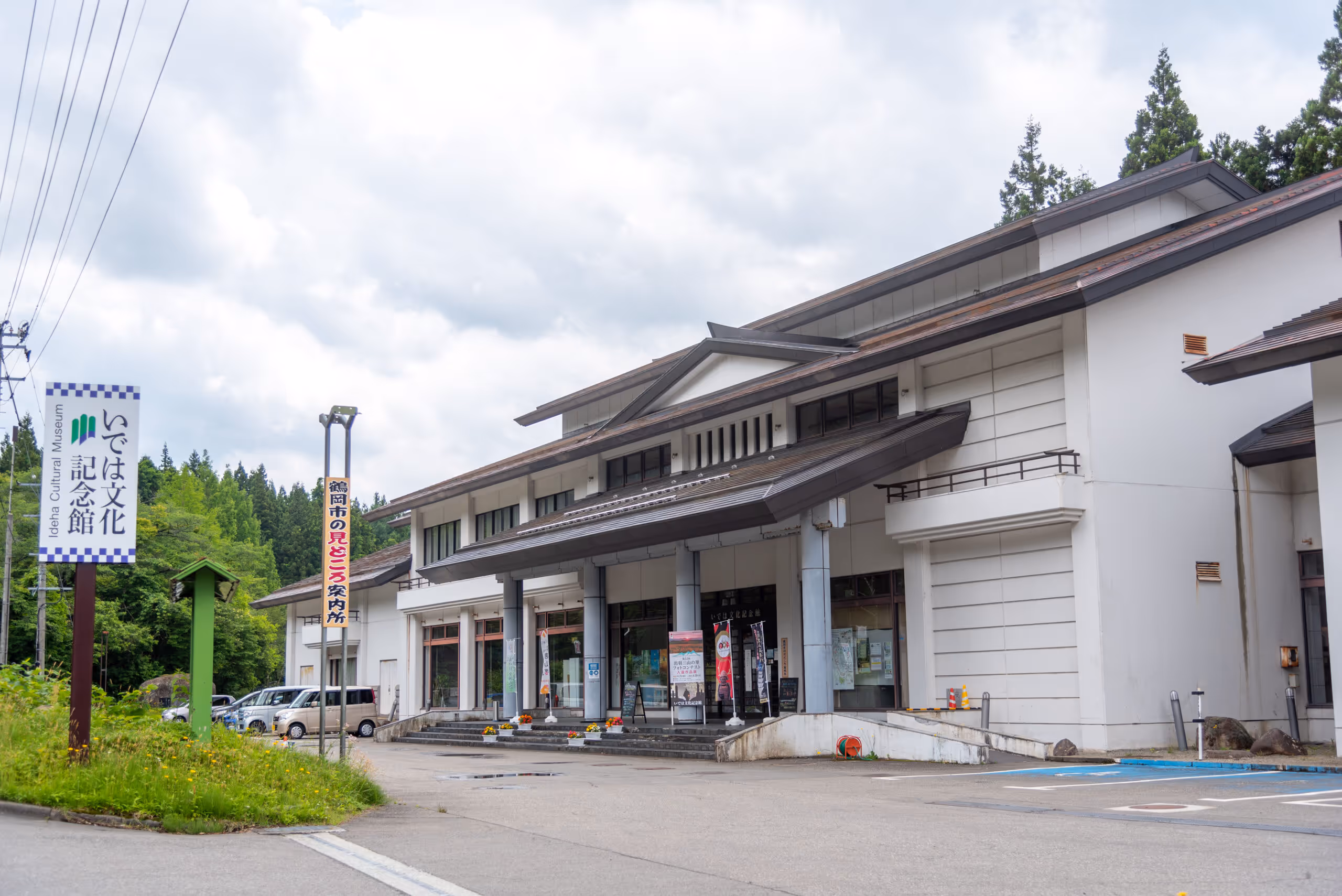 White building of Ideha Cultural Museum surrounded by greenery under a cloudy sky.