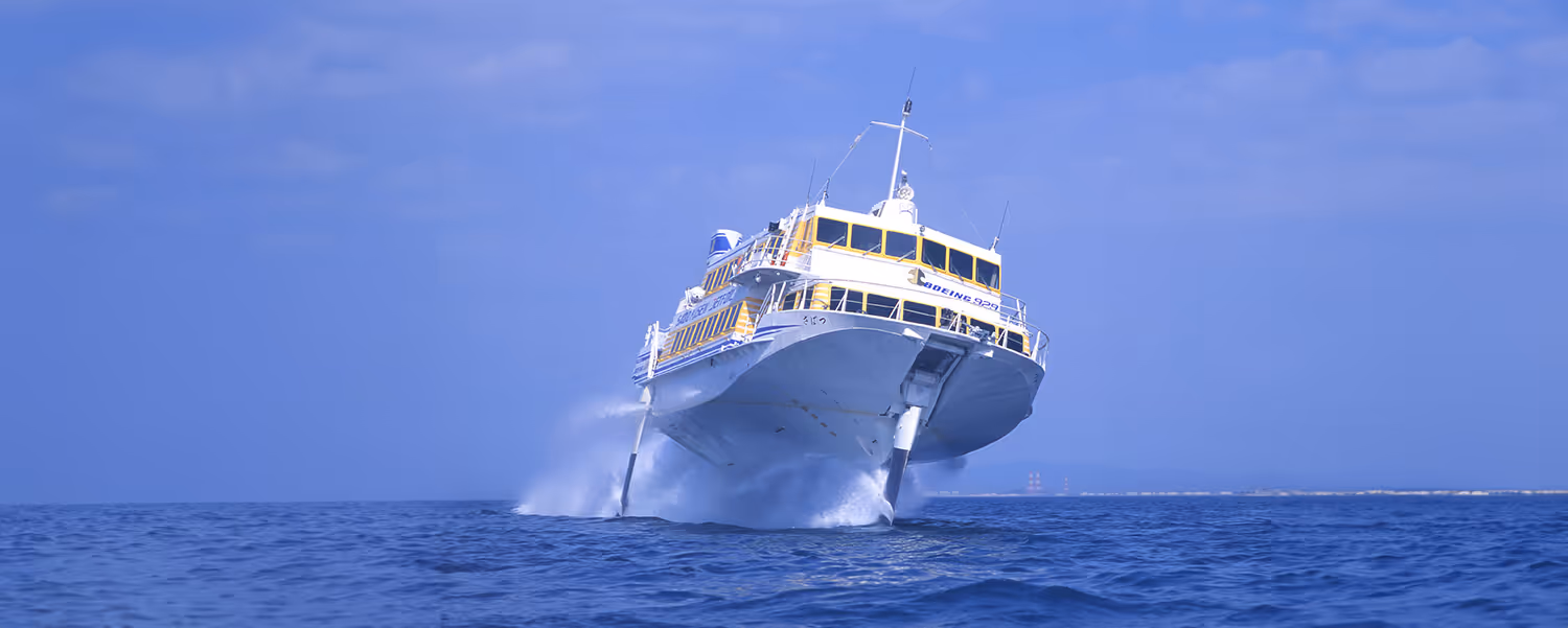 A white and yellow high-speed ferry riding above water with hydrofoils in the ocean under a blue sky.