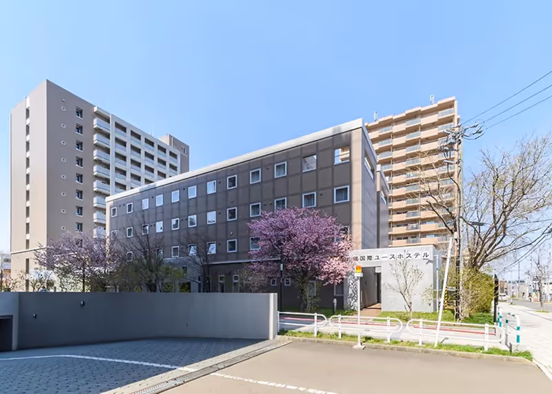 Modern multi-story buildings with purple blossoming trees in front under a clear blue sky.