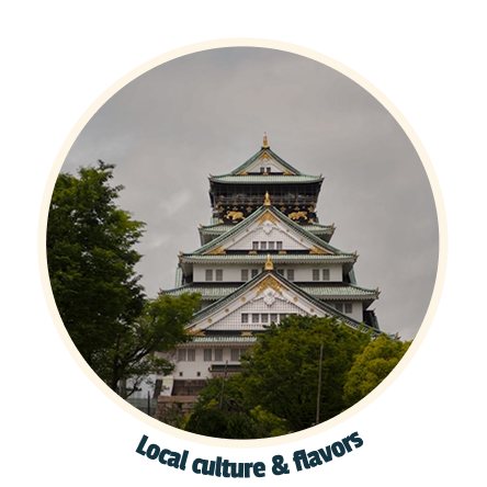 Osaka Castle in Japan surrounded by green trees under a cloudy sky.
