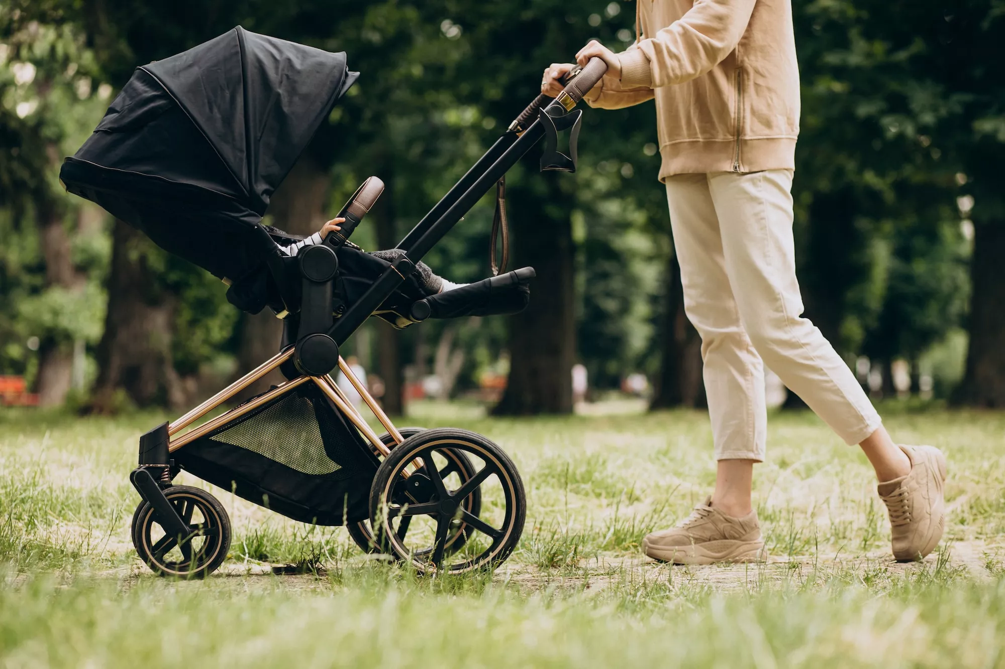 Parent pushing a stroller with a baby through a park
