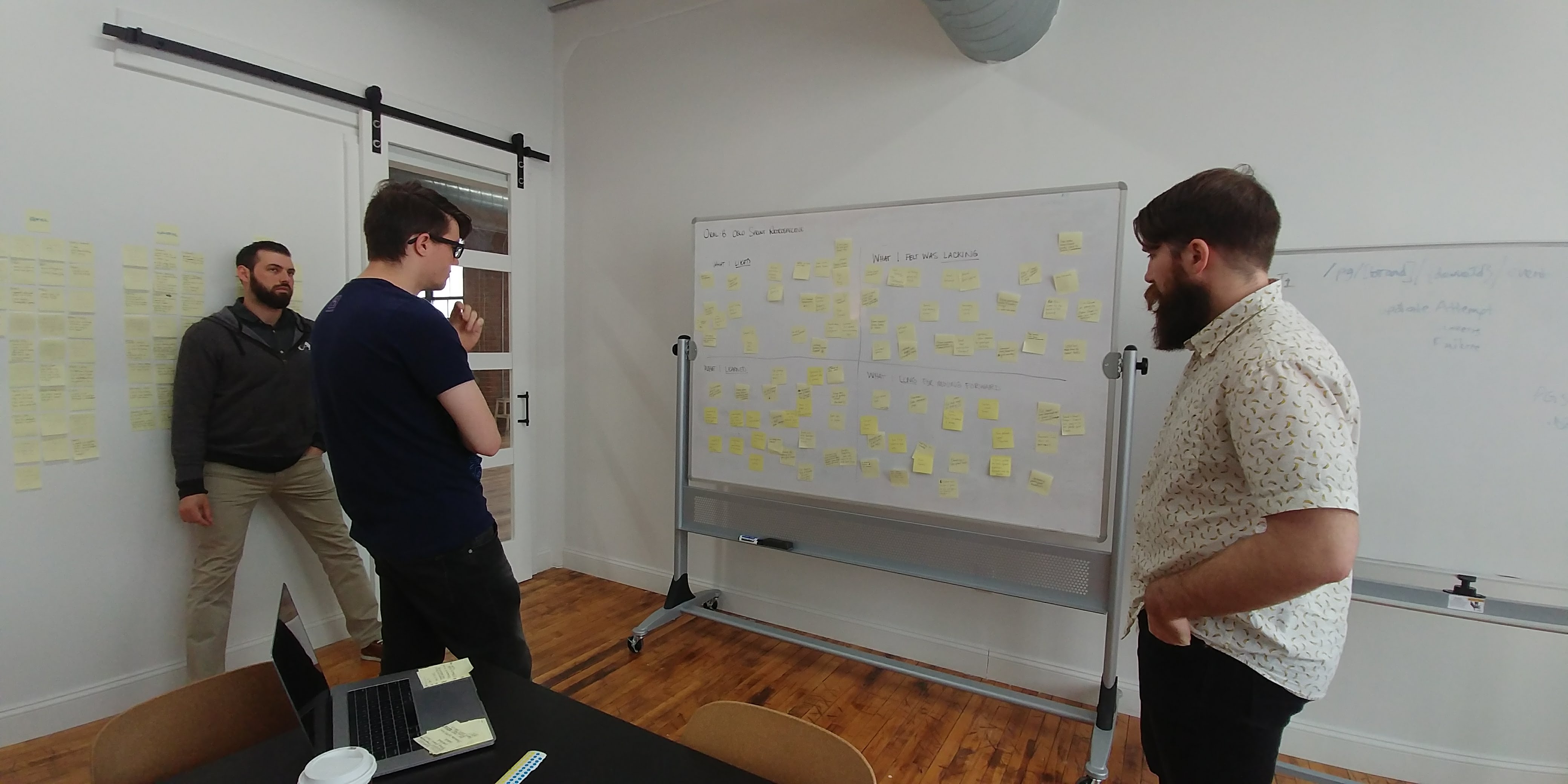 Three people standing in front of a whiteboard with lots of post-it notes reviewing the usability testing findings