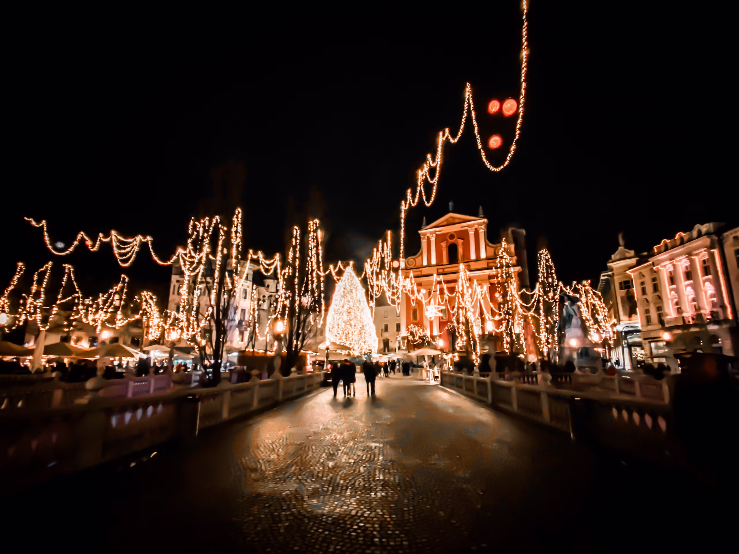 De verlichte kade langs de Ljubljanica tijdens Praznični december, met kraampjes langs het water