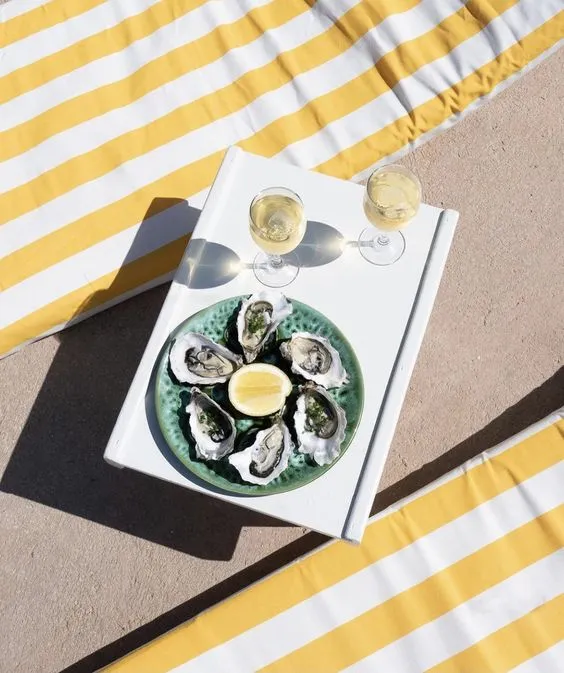 Oysters and drinks on table next to yellow striped pool towels