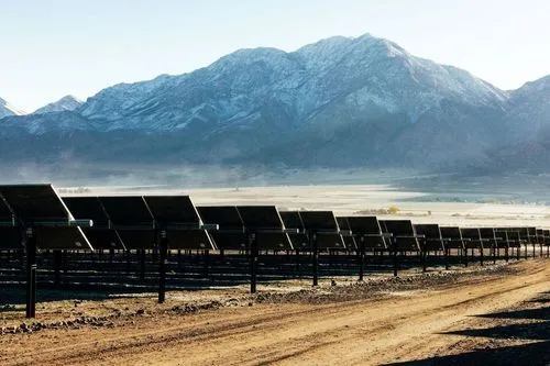 A row of solar panels facing a plain with a snow-capped mountain in the distance, at the Clover Creek Solar Project in Utah.