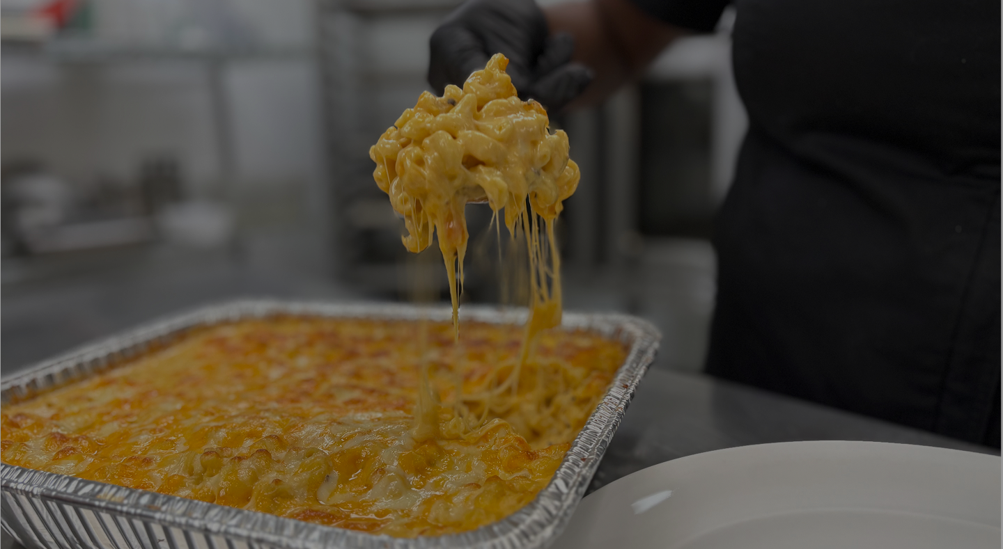 Pan of mac and cheese, hand not pictured is taking a scoop out of the tray.