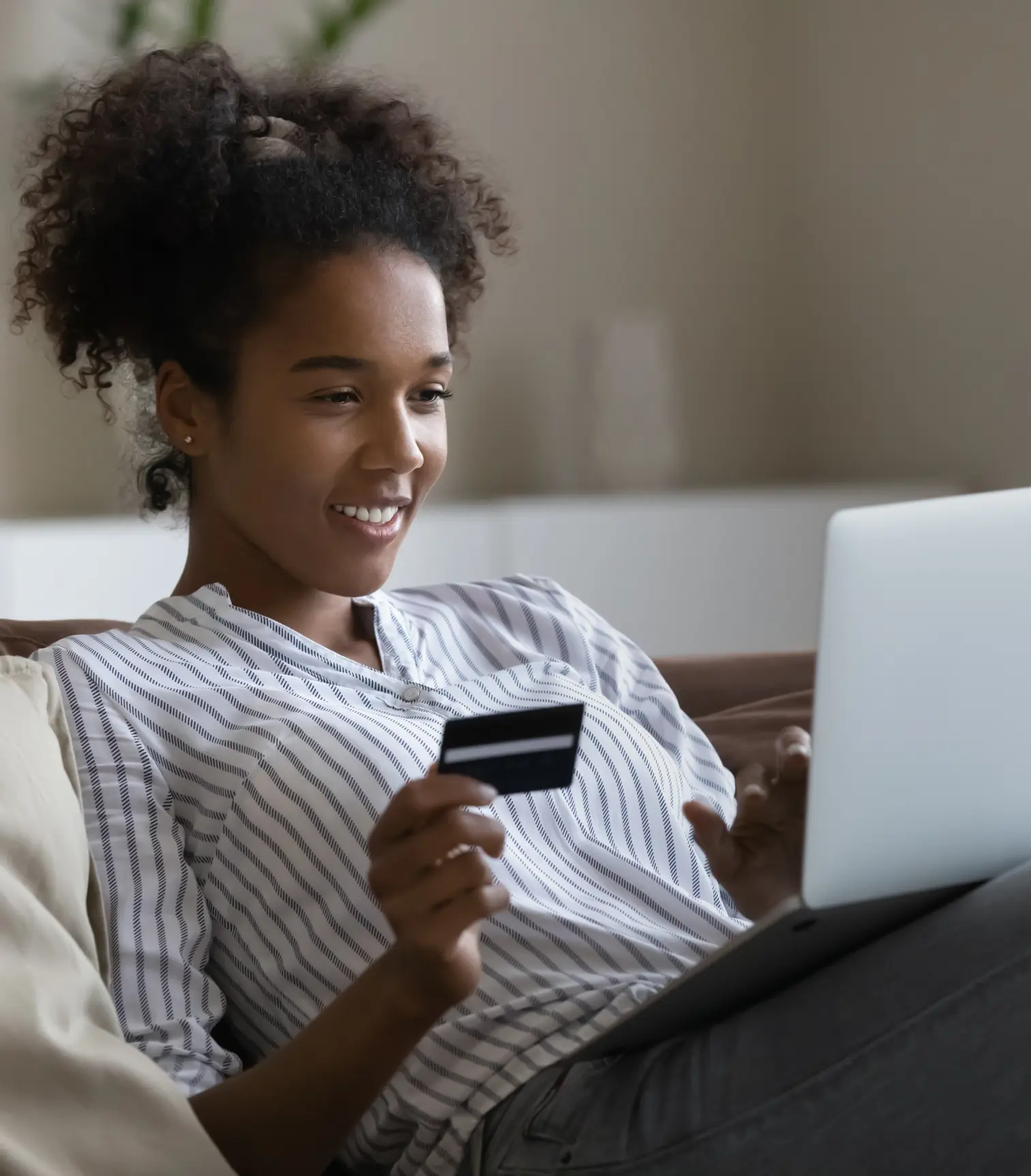 A teenage girl looking at her laptop while holding up a debit card, making online purchases