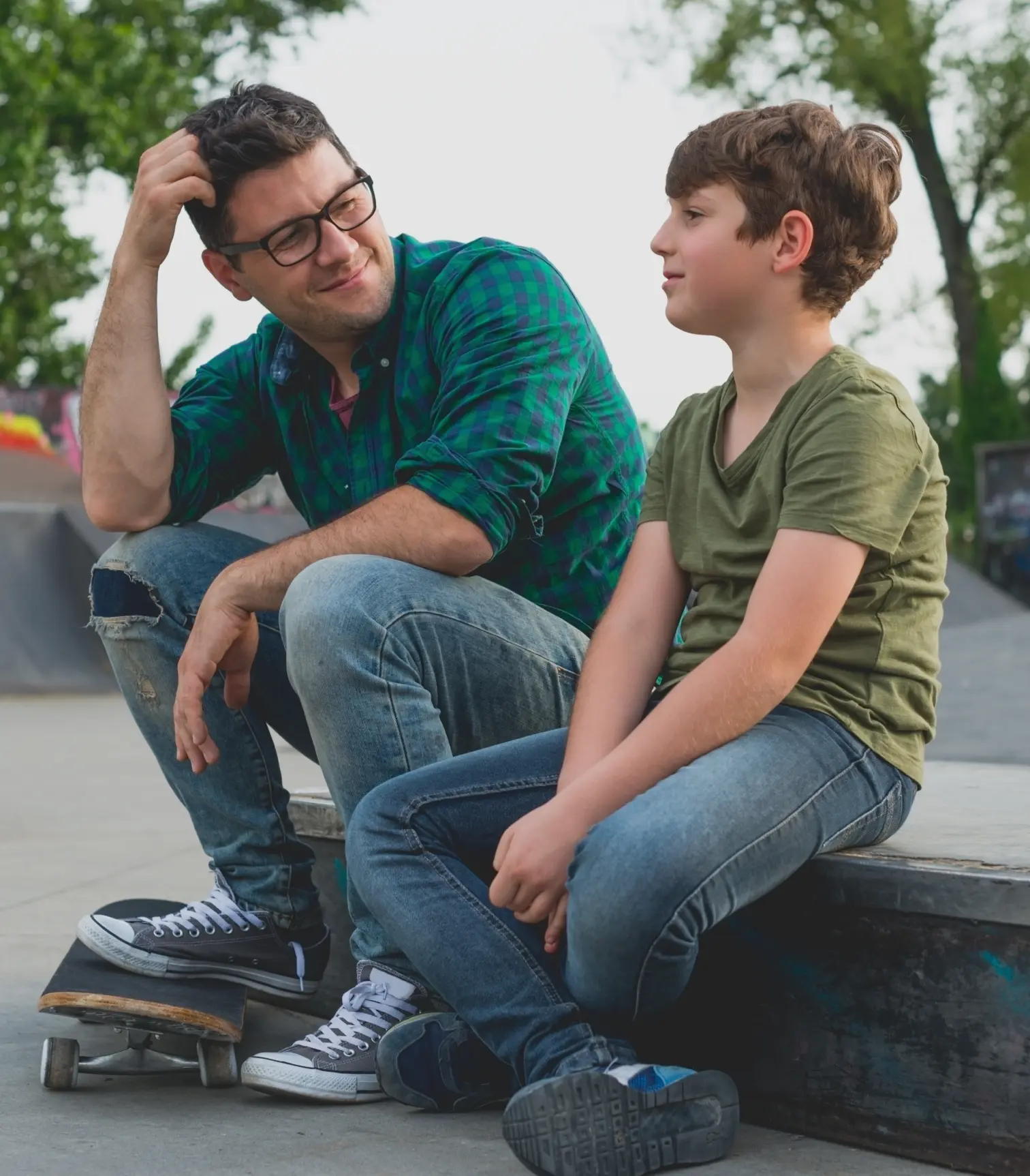 A young boy and his father sitting down at a skatepark and sharing a happy moment together