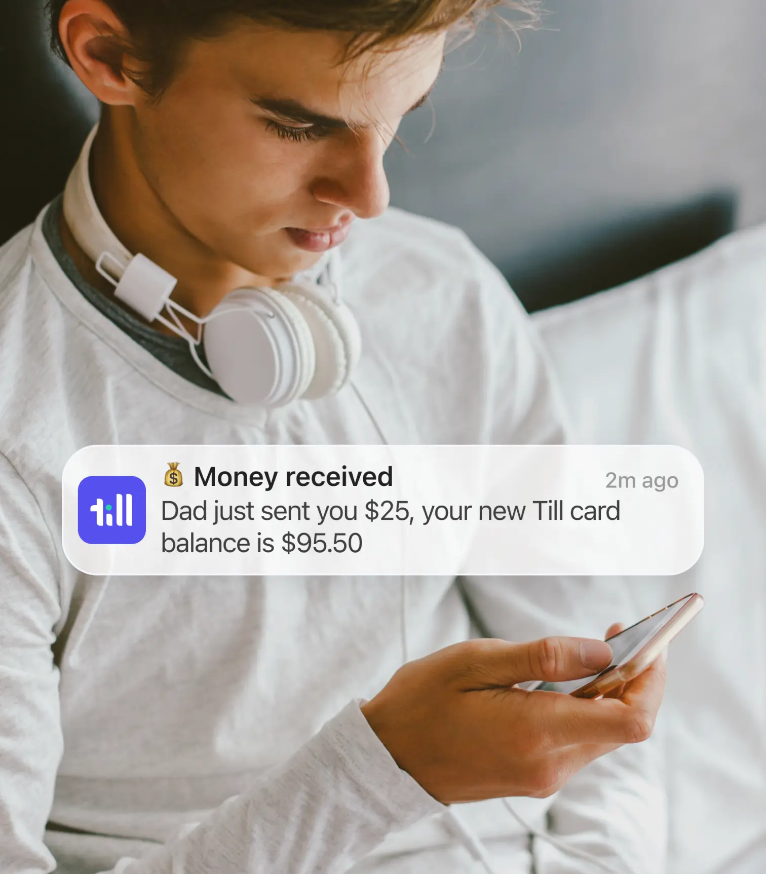 A teenage boy looking at a phone notification indicating that his father has sent money to his Till debit card