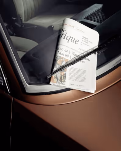 Newspaper placed under a windshield wiper on the front windshield of a car with tan and black interior.