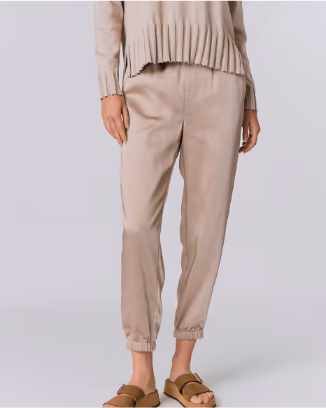 Person wearing beige tapered pants with elastic cuffs and a matching beige sweater, paired with brown sandals.