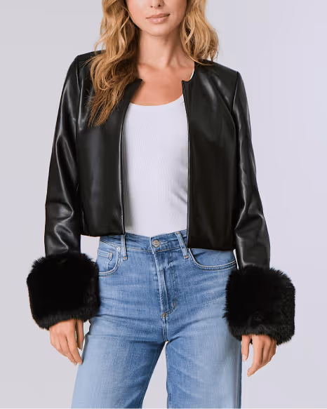 Woman wearing a black leather jacket with large black fur cuffs paired with a white ribbed tank top and blue jeans.