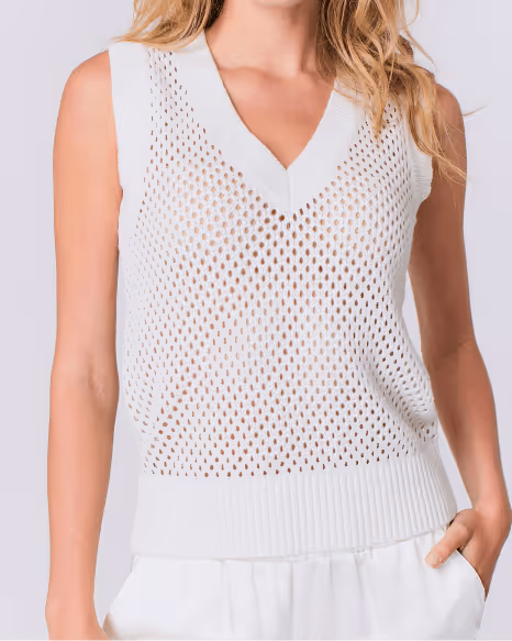 Woman wearing a white sleeveless V-neck knit sweater vest with a mesh pattern over white pants.
