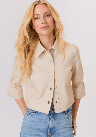 Woman in profile wearing a beige knitted sweater, white satin midi skirt, and brown sandals against a plain light gray background.
