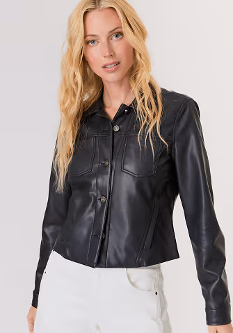 Woman with long blonde hair wearing a sleeveless beige knitted top and shiny light brown wide-leg pants, standing with arms crossed.