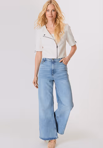 Blonde woman with wavy hair wearing a sleeveless tan knit sweater with geometric patterns.