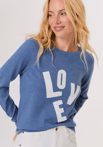 Blonde woman wearing a light brown satin short-sleeve zip-up jacket over a white top and matching light brown pants.