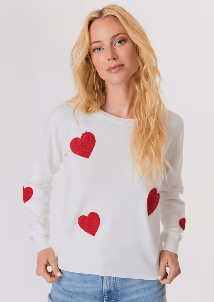 Woman with blonde hair wearing a cream V-neck sweater over a white button-up shirt and light blue jeans.