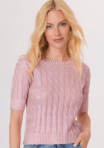 Blonde woman wearing a cream jacket with large fluffy white cuffs over a white top and white pants.