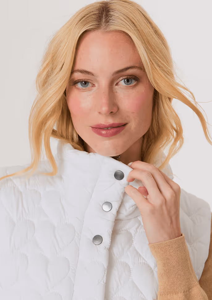 Blonde woman wearing a beige cardigan with furry cuffs and light blue high-waisted jeans.