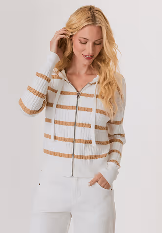 Blonde woman wearing a light gray sweater adorned with small pearls, posing against a plain light background.