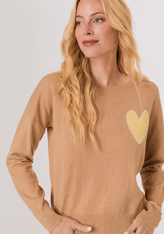 Woman wearing a white sweater with small bead embellishments paired with blue jeans, looking to the side.