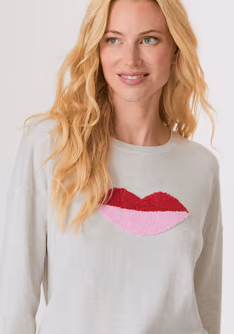 Woman wearing a white sleeveless V-neck knit sweater vest with a mesh pattern over white pants.