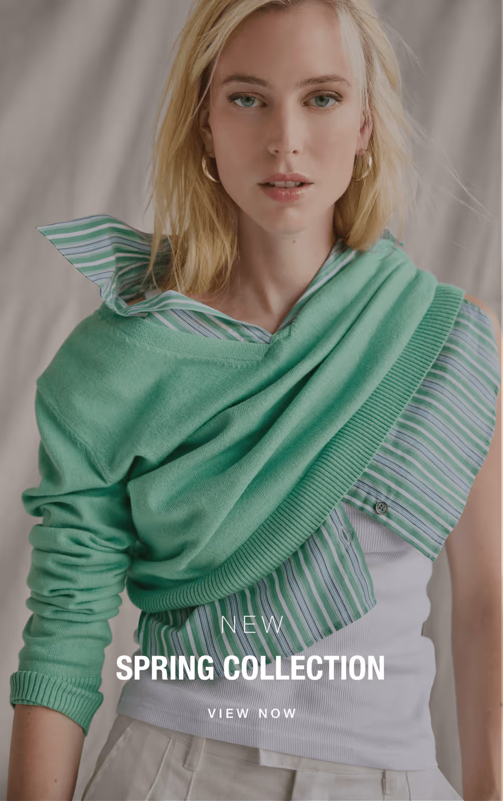 Blonde woman wearing a green sweater draped over a striped green and white shirt, promoting new spring collection.