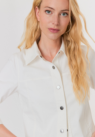 Blonde woman with wavy hair wearing a sleeveless tan knit sweater with geometric patterns.