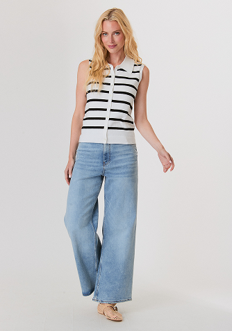 Woman in profile wearing a beige knitted sweater, white satin midi skirt, and brown sandals against a plain light gray background.