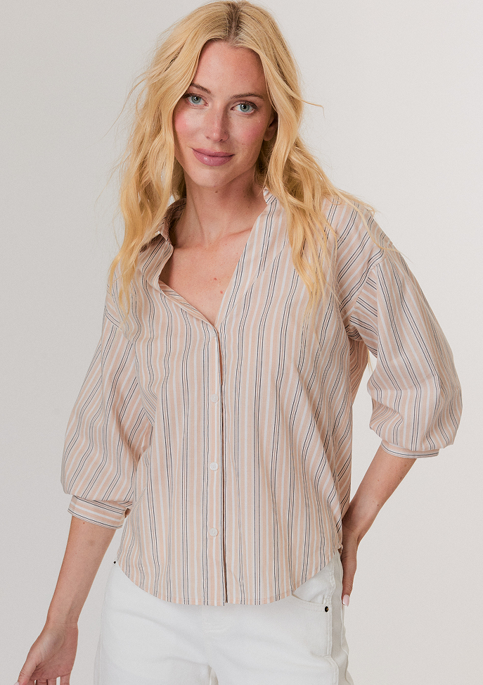 Blonde woman wearing a shiny gold short-sleeve puffer jacket with a zipper, paired with white pants.