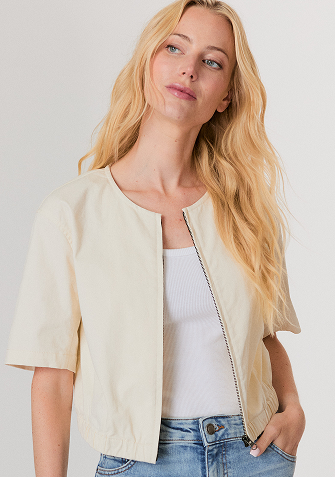 Blonde woman in a navy button-up shirt with embellished collar and light blue jeans against a plain background.