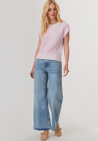 Woman wearing a black leather jacket with large black fur cuffs paired with a white ribbed tank top and blue jeans.