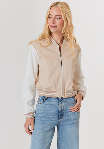 Woman with blonde hair wearing a white button-up blouse and wide-leg blue jeans standing against a light gray background.