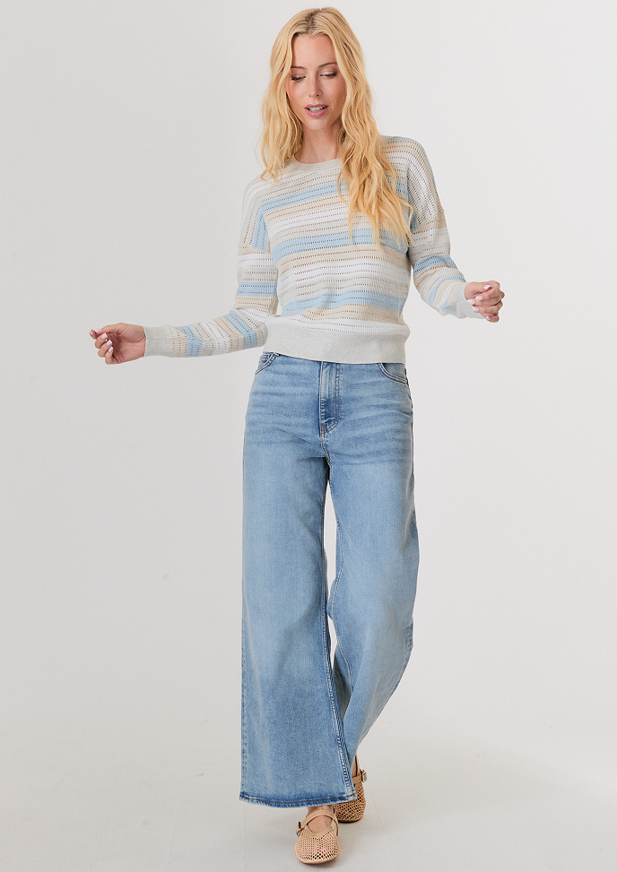 Woman with blonde hair wearing a cream V-neck sweater over a white button-up shirt and light blue jeans.