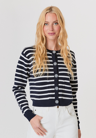 Blonde woman wearing a beige long-sleeve sweater with a pleated hem and blue jeans against a plain light gray background.