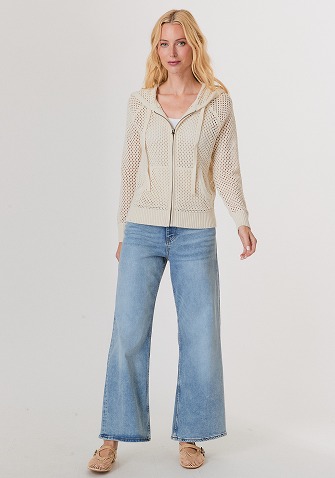 Blonde woman wearing a black short-sleeve jacket over a white top and matching black pants against a light gray background.