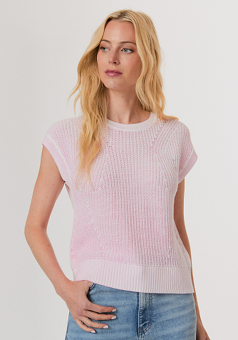 Woman wearing a red sweater with white and red star patterns, paired with white pants, standing against a light background.