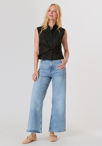 Woman wearing a white long-sleeve top with fluffy cuffs and blue wide-leg jeans, standing against a plain background.