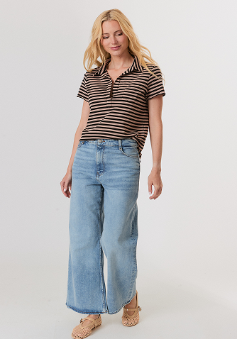 Blonde woman in a navy button-up shirt with embellished collar and light blue jeans against a plain background.
