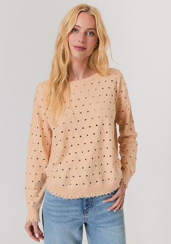 Blonde woman wearing a black short-sleeve open jacket over a white sleeveless top and white pants, standing against a light gray background.