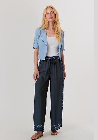 Blonde woman wearing a black and white sweater with a snowflake pattern and blue jeans standing against a light gray background.