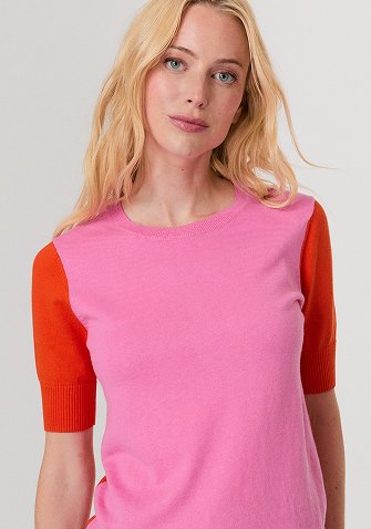 Woman wearing a red sweater with white and red star patterns, paired with white pants, standing against a light background.