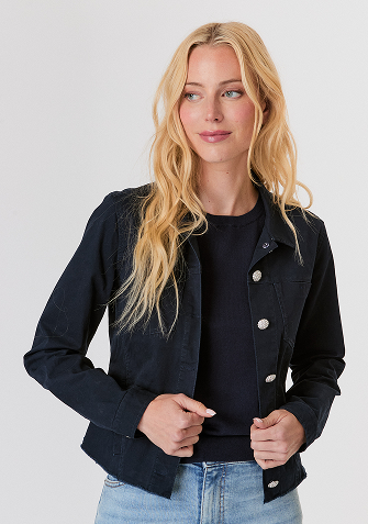 Blonde woman wearing a red knit sweater and white pants standing against a plain light background.