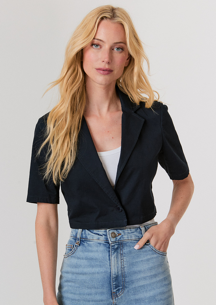 Blonde woman wearing a dark brown cropped cardigan with a satin ribbon tie over a white top and light blue high-waisted jeans.